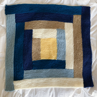 A modern log cabin knitted baby blanket in blue, yellow, and cream Wooly Worsted merino wool.
